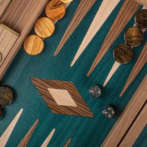 May include: A close-up of a backgammon board with wooden game pieces and dice. The board features a teal playing surface with wooden triangles and a diamond-shaped inlay. The wooden game pieces are light and dark brown.