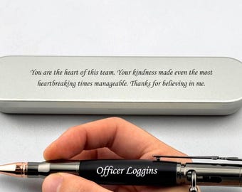 May include: A black bolt-action pen with rose gold accents and the engraved text Officer Loggins, positioned in front of a silver metal case featuring the engraved text: You are the heart of this team. Your kindness made even the most heartbreaking times manageable. Thanks for believing in me.