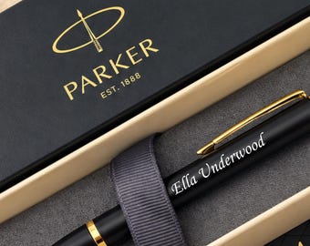 May include: A matte black Parker IM ballpoint pen with gold-tone accents and a gold clip, engraved with the name Ella Underwood. The pen is secured by a grey ribbon inside a black and beige presentation box featuring the Parker logo and text.