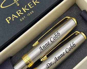 May include: Two silver-toned Parker Sonnet pens with gold-colored clips and accents, presented in a branded box. One pen is engraved with the name Anne Cobb, and the other is engraved with the title and name Dr. Anne Cobb in a dark script font.