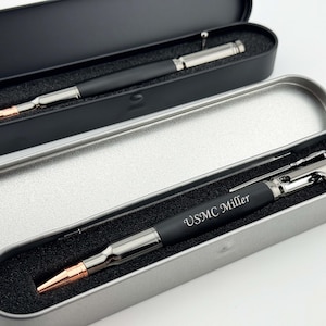 May include: Two black and silver bullet pens in their individual metal cases. One pen is engraved with "USMC Miller".