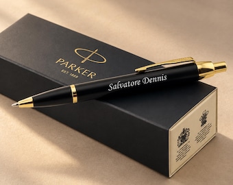 May include: A black ballpoint pen with gold-colored accents and a gold clip, featuring the name Salvatore Dennis engraved on the barrel. The pen rests on a black rectangular Parker gift box with gold text and logos printed on the lid and side.