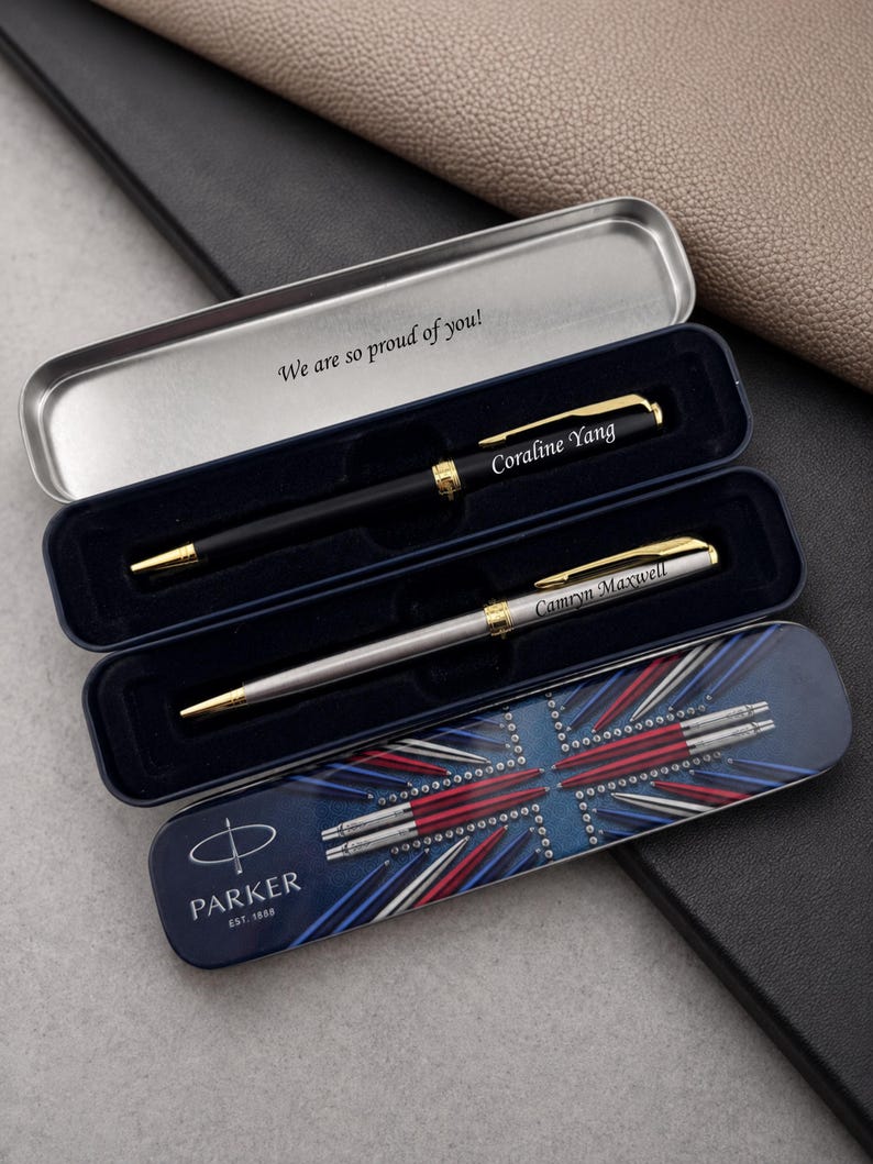 May include: Two Parker pens in a metal case. One pen is matte black with gold accents and the name Coraline Yang. The other is silver with gold accents and the name Camryn Maxwell. The case lid features a Union Jack design and the text We are so proud of you!