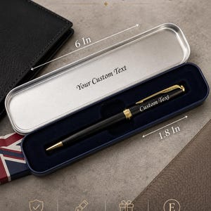 May include: A black ballpoint pen with gold-tone accents and a twist mechanism, resting in a navy blue lined metal case. The case measures 6 inches by 1.8 inches. The pen features the text Custom Text, and the case lid reads Your Custom Text.