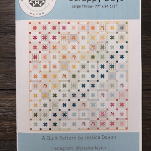Könnte beinhalten: Ein Quiltmuster mit dem Titel "Scrappy Days" von Jessica Dayon. Das Muster ist für einen großen Überwurf von 195.6 cm x 214.6 cm. Das Quilt-Design zeigt ein Patchwork aus bunten Quadraten mit Sternmotiven. Die Musterdetails befinden sich auf hellblauem Hintergrund.