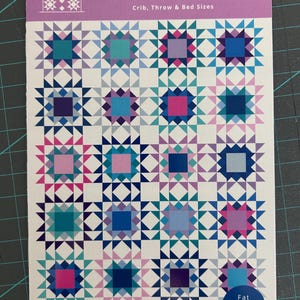 May include: A quilt pattern booklet titled STAR DEW 12, featuring a grid of sixteen colorful star blocks in shades of blue, purple, and pink. The cover includes the text Quilt Cakes, Crib, Throw & Bed Sizes, and Fat Quarter Friendly.