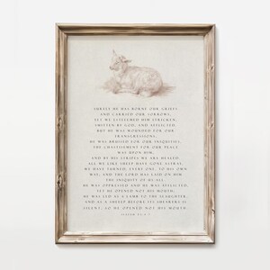 May include: A framed print featuring a sepia-toned illustration of a lamb lying down, with text from Isaiah 53:4-7. The wooden frame adds a rustic touch to the artwork, suitable for home decor. The print is a religious themed item.