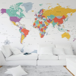 Puede incluir: Un sofá blanco con dos almohadas blancas y una alfombra blanca delante. La pared detrás del sofá tiene un mapa del mundo colorido con los nombres de los países etiquetados en texto negro.