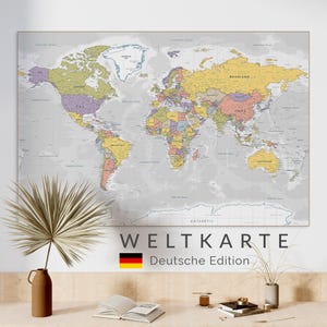 May include: A large, colorful world map with country borders and names, mounted on a wall. The map has a neutral gray background with countries in various colors. Text at the bottom reads "WELTKARTE Deutsche Edition" with a German flag.