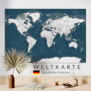 May include: A large world map with a dark blue ocean background and white landmasses. The map is labeled with country names and features the text "WELTKARTE Deutsche Edition" and a German flag. The map is displayed on a white wall.