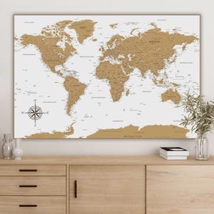 May include: A white world map with brown continents and country borders. The map is framed and hanging on a wall above a wooden dresser.