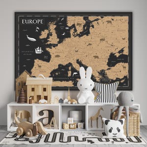 Può includere: Una mappa dell'Europa nera e marrone con un contorno bianco del continente e la parola "EUROPA" in bianco in alto. La mappa è appesa a un muro bianco in una cameretta con uno scaffale bianco sotto. Lo scaffale è decorato con giocattoli di legno, tra cui una casa, un'auto, una giraffa e un orso panda.