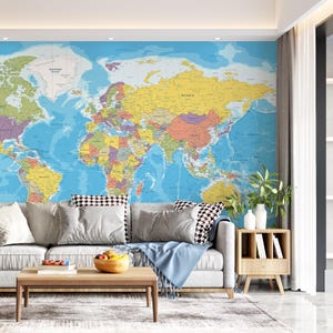 May include: A large, colourful world map mural adorns a living room wall. The map, with countries in various colours, is above a grey sofa with cushions. A wooden coffee table and side table complete the room's decor.