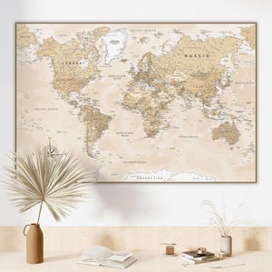 Puede incluir: Un mapa del mundo enmarcado en tonos beige y marrón, con detalles geográficos y nombres de países. El mapa incluye una rosa de los vientos y se muestra sobre un escritorio con objetos decorativos.