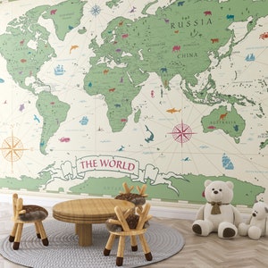 Könnte beinhalten: Ein Kinderzimmer mit einer großen Weltkarte in Grün- und Beigetönen. Ein Holztisch und zwei Stühle mit Hirschgeweih-Rückenlehnen stehen auf einem grauen Teppich. Zwei Teddybären sitzen in der Nähe der Wand, was eine spielerische Lernumgebung schafft.