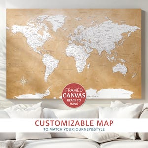 Peut inclure: Une carte du monde encadrée sur toile avec un fond beige et des continents en relief blanc. La carte comprend une rose des vents et le texte "CUSTOMIZABLE MAP" et "FRAMED CANVAS READY TO HANG".