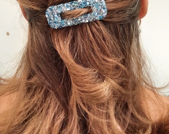 Puede incluir: Una mujer con el pelo largo y castaño lleva una camisa negra. Lleva una pinza para el pelo azul con purpurina en el pelo.