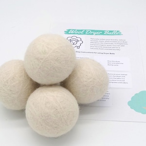 May include: Four white wool dryer balls. The balls are made of natural wool and are designed to help reduce drying time and soften clothes. The image also includes a card with instructions for using the dryer balls.