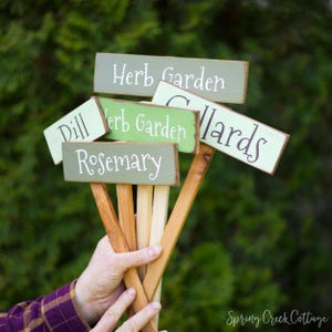 Peut inclure: Ensemble de panneaux de jardin d'herbes aromatiques en bois avec lettrage blanc. Les panneaux sont peints dans des tons de vert et de marron, avec les mots "Herb Garden", "Dill", "Rosemary" et "Collards".