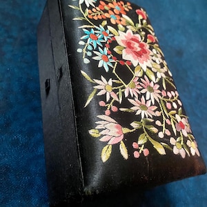 May include: Black rectangular box with a floral embroidery design. The embroidery features pink, red, blue, and orange flowers with green leaves. The box has a small clasp closure.