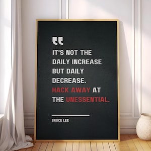 May include: Black and white motivational quote poster with a gold frame. The quote reads "It's not the daily increase but daily decrease. Hack away at the unessential." - Bruce Lee.