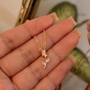 Peut inclure: Un d&eacute;licat collier dor&eacute; avec un pendentif en forme de tulipe. Le pendentif pr&eacute;sente un bouton de tulipe d&eacute;taill&eacute; et deux feuilles orn&eacute;es de petites pierres pr&eacute;cieuses transparentes. La cha&icirc;ne est de conception fine et torsad&eacute;e.