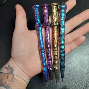 May include: Four metallic pens with iridescent finishes in shades of blue, purple, gold, and green. The pens have a textured, almost wood-like appearance.