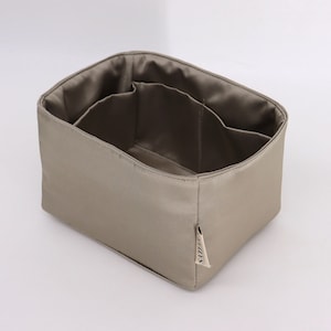 May include: A beige fabric organizer with multiple compartments and a small label that says "Savor" on the side.