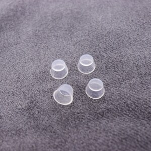 May include: Four clear plastic caps, possibly for bottles or jars, are arranged on a gray fabric surface.