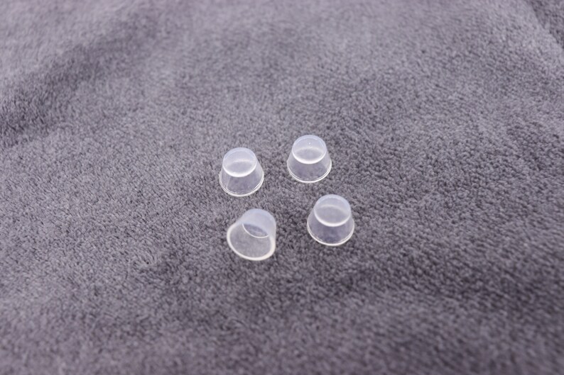 May include: Four clear plastic caps, possibly for bottles or jars, are arranged on a gray fabric surface.