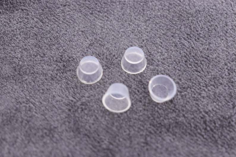 May include: Four clear plastic cups, possibly for mixing paint or other small crafts, are arranged on a gray fuzzy surface.