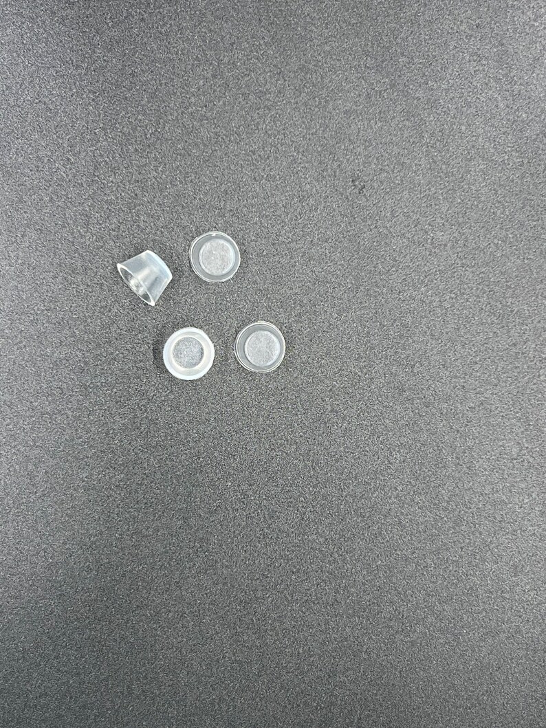 May include: Four clear plastic bottle stoppers with a small white filter inside each stopper.