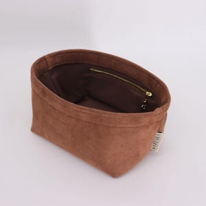 May include: A brown suede bag with a zipper closure and a small label that says "VIZARA".