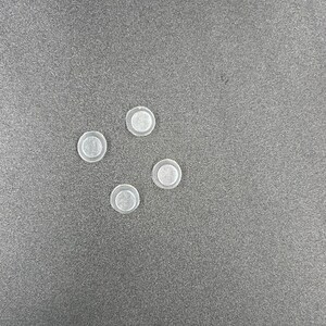 May include: Five clear plastic round buttons, arranged in a semi-circle pattern on a gray surface.