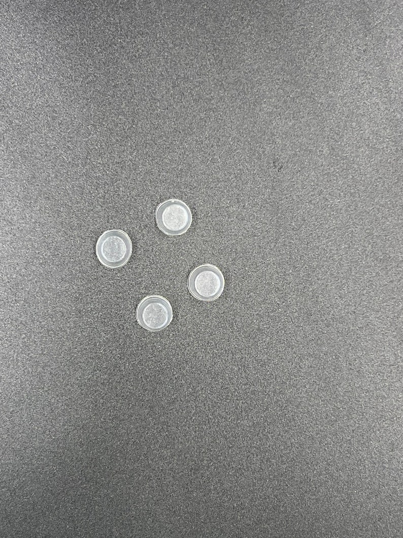 May include: Five clear plastic round buttons, arranged in a semi-circle pattern on a gray surface.