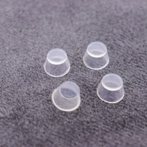 May include: Four clear plastic caps, possibly for bottles or jars, are arranged on a gray fuzzy surface.
