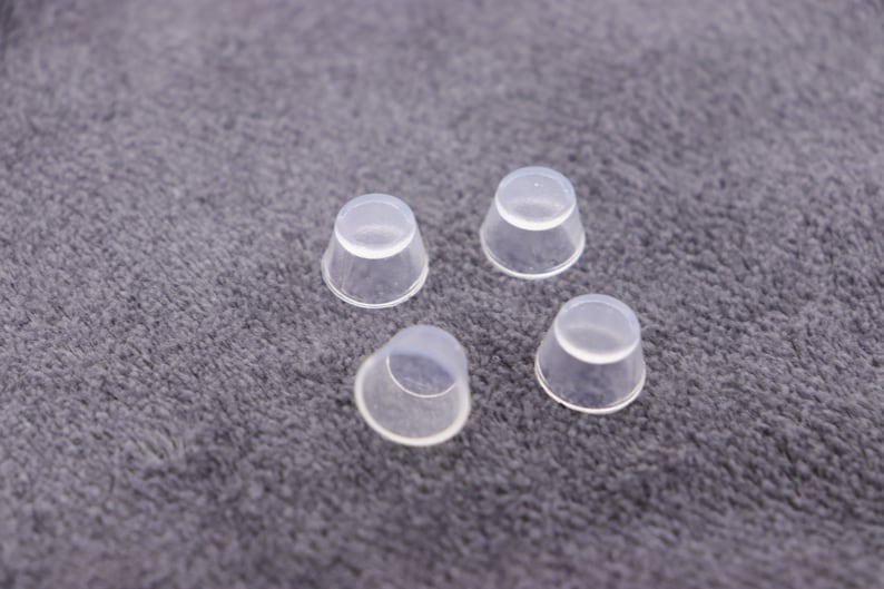 May include: Four clear plastic caps, possibly for bottles or jars, are arranged on a gray fuzzy surface.