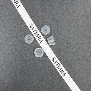 May include: Four clear plastic bottle stoppers on a gray surface with a white ribbon that says "SATIARA" on it.