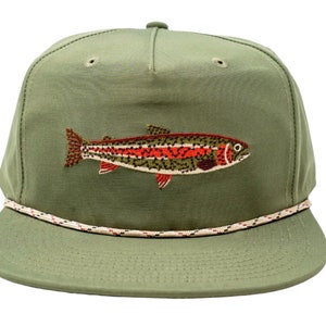 May include: Olive green flat-brimmed cap featuring an embroidered trout design. The trout is detailed with red, orange, and green accents. The cap has a white and red rope detail around the brim, and a button on top.