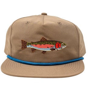 May include: A tan baseball cap with a blue rope brim and a colorful embroidered fish patch. The fish features red, blue, green, and yellow details. The cap has a rounded crown and a flat brim.