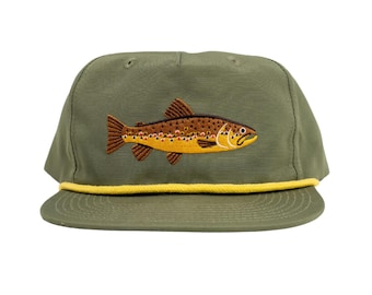 May include: An olive green baseball cap with an embroidered brown and yellow trout design. The cap has a yellow rope detail around the brim. A stylish accessory for fishing enthusiasts or those who appreciate outdoor themes.