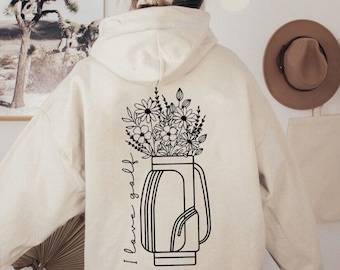 May include: A cream-colored hoodie with a black outline of a golf bag with flowers coming out of the top. The text "I love golf" is written on the side of the bag.