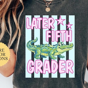 May include: A dark gray t-shirt with a graphic that says "Later Fifth Grader." The design features a cartoon alligator in front of light blue stripes and pink text. The shirt also has the word "PEPPER" printed on the top right.