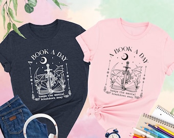 May include: Two t-shirts, one heather navy and one pink, with a graphic design of a book, sword, and dragon. The text on the shirts reads "A Book A Day Keeps The Mental Breakdown Away".