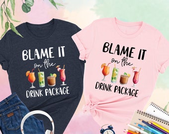 Könnte beinhalten: Zwei T-Shirts, eines in Marineblau und eines in Pink, mit dem Text "Blame it on the drink package" und einer Grafik von vier Cocktails.