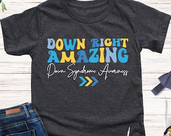 May include: Dark heather grey t-shirt with the text "Down Right Amazing" in colorful letters. The text "Down Syndrome Awareness" is written below the main text with two yellow arrows pointing to the right.