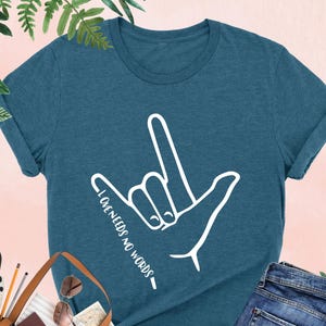 May include: A teal blue t-shirt with a white hand sign and the text "LOVE NEEDS NO WORDS".