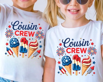 Op de afbeelding: Twee kinderen dragen witte t-shirts met de tekst "Cousin Crew" in blauwe letters. De shirts hebben patriottische ijsje en vuurwerkgraphics in rood, wit en blauw. De kinderen dragen zonnebrillen.