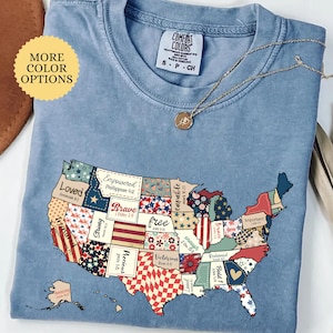 May include: A blue jean t-shirt with a patchwork design of the United States. Each state is a different color and pattern, with words and bible verses printed on each state. The words include "Loved", "Empowered", "Brave", "Free", "Treasured", "Strong", "Precious", "Victorious", "Redeem", "Bold", "Capable", "Enough", "Important", and "Joyful".