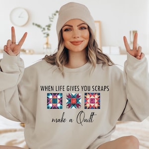 May include: A beige sweatshirt with the text "WHEN LIFE GIVES YOU SCRAPS make a Quilt" and three colorful patchwork quilt squares.